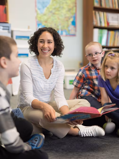 Eine Schulbegleiterin liest mit einer Gruppe von Schülerinnen und Schülern ein Buch.